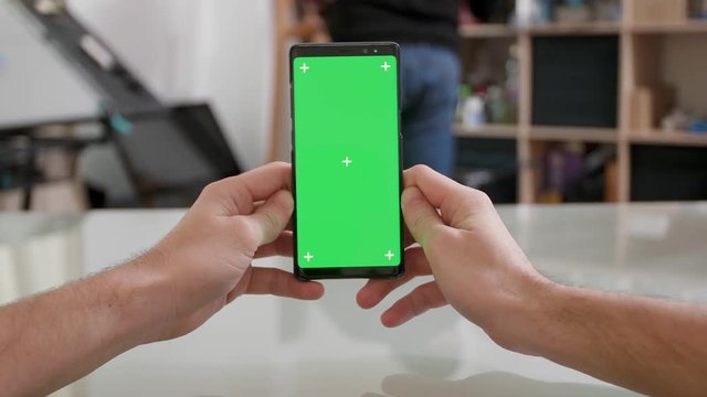 Mans point of view holding a smartphone vertically with green screen on. Watching a video on th internet during a break.