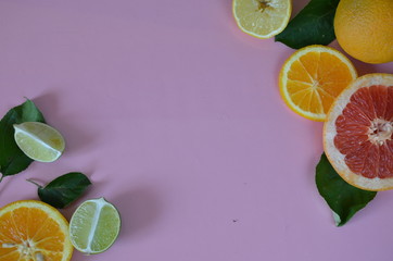 Flat lay of citrus fruits like lime and lemon with lemon tree leaves on light pink background making a frame