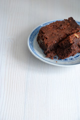 Vertical top view of brownie in blue and white dish. On white wooden background with copy space