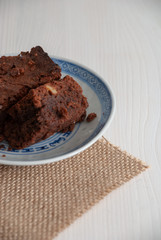 Vertical top view of brownie in blue and white dish. On burlap cloth and white wood background with copy space