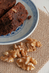Vertical top view of brownie with nuts in blue and white dish. On burlap cloth and white wood background