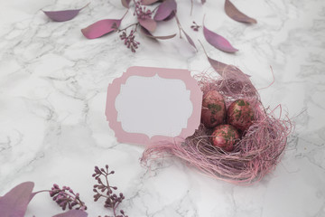 easter pink eggs in a nest with spring flowers on a marble background. Place for inscription. top view