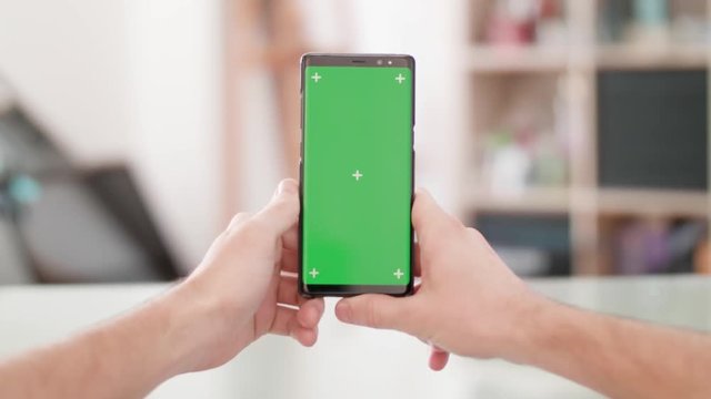 Man;s point of view holding a smartphone vertically with green screen on in the center of the frame. Man holds a smartphone.