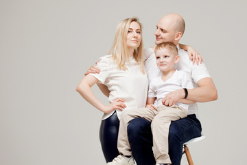 Mom dad and son, young family portrait on light grey background.