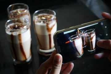An Indian Woman's hand taking photos of milkshake in glass on her mobile phone.