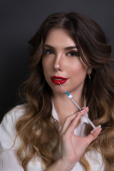 Obraz premium Doctor in a pink polo with a syringe. Beautician, cosmetologist on a gray background. Beautiful girl, nurse. Medicine, beauty industry.