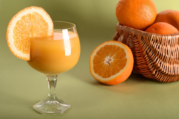 Orange juice in a glass with orange wedge on side on green background	