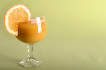Orange juice in a glass with orange wedge on side on green background	