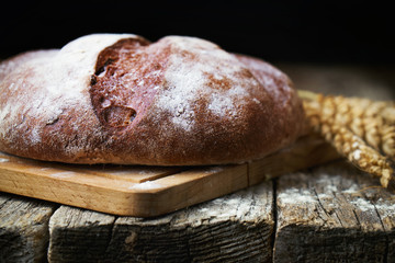 Round bread and wheat ears on the old wooden table