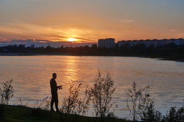 Angler  on the river Bank against the sunset sky.