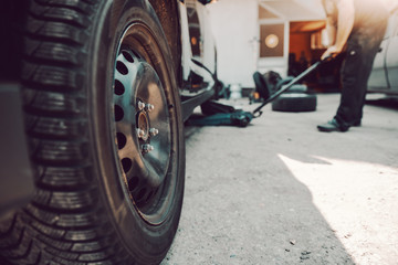 Auto mechanic using car jack at workshop. Selective focus in tire.