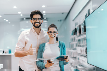 Young attractive multicultural couple looking for new plasma tv. Woman holding brochure while man...