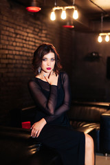 Fototapeta na wymiar portrait of a beautiful brunette girl in a black dress in a dark room 1