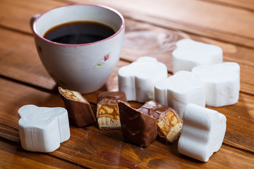 white cup of black coffee, chocolate with nuts on a wooden board with marshmallows
