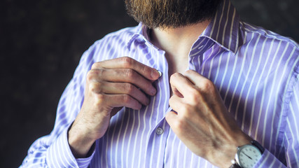 Closeup of Young Bearded Man in Wristwatch Buttoning His Striped Shirt Getting Ready to Go Out. Be Late for Work, Dressed in a Hurry Concept.