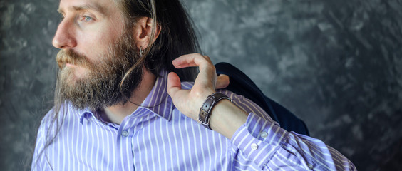Fashion Stylish Male with Beard and Long Hair in Striped Shirt and Wristwath Holding His Jacket on...