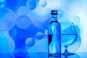 transparent glass and bottle with water and oily drops on azure background 