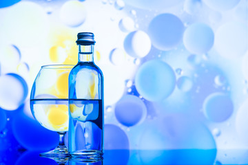 transparent glass and bottle with water and oily drops on azure background 