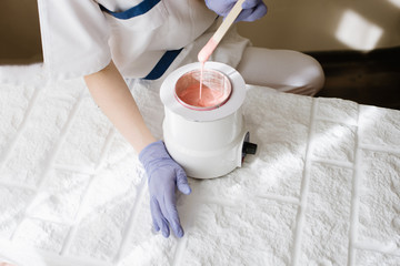 Hot wax bowl and hands on table in spa center close up. view from the top