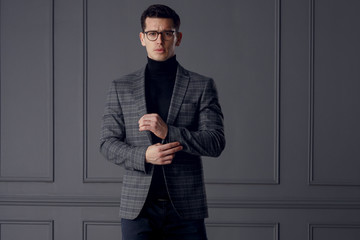 Confident bussinesman wear stylish gray suit and black eyeglasses looks with attitude, on gray wall...