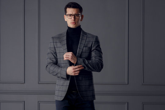 Confident bussinesman wear stylish gray suit and black eyeglasses looks with attitude, on gray wall background.
