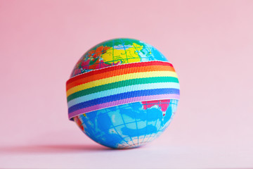 globe with LGBT rainbow ribbon on pink background