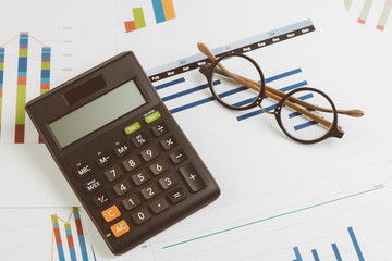 Naklejka na ściany i meble Black calculator, eyeglasses on monthly graph and chart on office table using as company profit and loss, financial and accounting activities