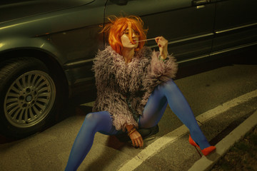 Young attractive girl in a red wig defiantly posing at a gas station.