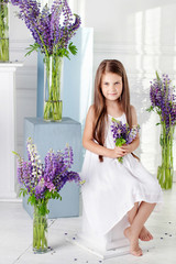 Beautiful little emotional girl sits among violet flowers. A flower decor in an interior