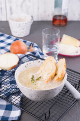 Onion soup with cheese and croutons in a white cup on a gray stone background. Traditional french soup in light colors. Country food. Free space for text