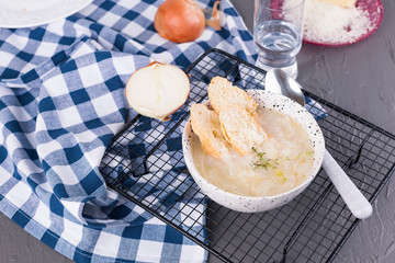 Onion soup with cheese and croutons in a white cup on a gray stone background. Traditional french soup in light colors. Country food. Free space for text