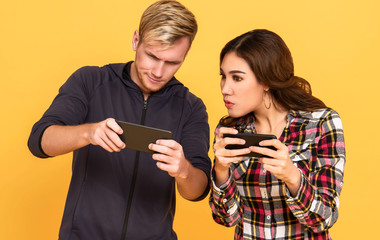 excited people man and woman while both using mobile phones play game over yellow background.