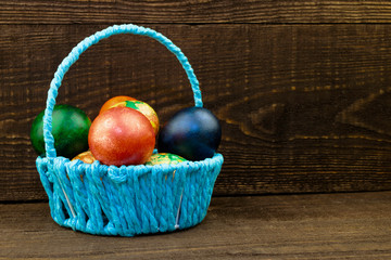 blue basket with easter eggs on a dark brown wooden background, copy space