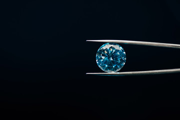 colorful blue sparkling diamond in tweezers isolated on black - obrazy, fototapety, plakaty