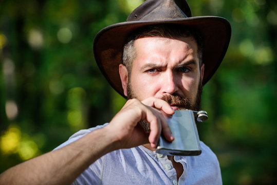 Wild West Is His Heart. Camping And Hiking. Mature Male With Brutal Look Drink Alcohol From Flask. Bearded Man In Cowboy Hat In Park Outdoor. Man Hipster Relax In Autumn Forest. Spring Sunny Weather