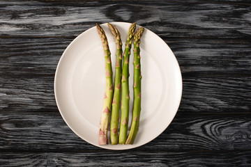 top view of organic asparagus on plate on grey wooden background