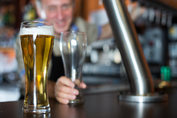 glass of beer on bar counter against background of friendly bartender