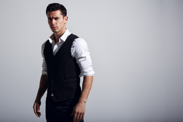 Young handsome man wearing white shirt, black vest, standing near grey wall. Studio portrait, isolated on gray background. Horizontzal view.