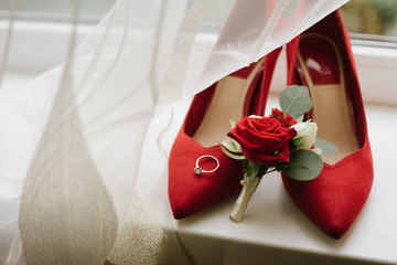 Wedding rings on red women's shoes near the red rose buttonhole on the window. wedding concept