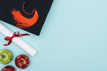 Top view of academic cap, diploma and apples on blue surface