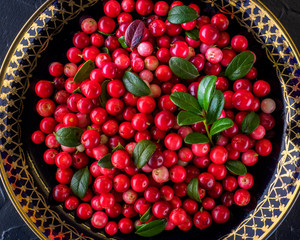 Berries on a plate on a dark background in a rustic style. National cuisine. raw materials for tea, jam and medicinal decoctions. Vaccinium vitis-idaea (lingonberry or cowberry).