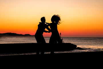 Fototapeta na wymiar Couple dancing on the pier during sunrise make for awesome silhouettes