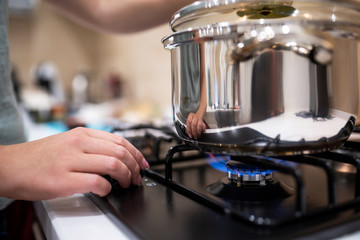 Beautiful young woman housewife prepairing dinner, hold in hands big steel saucepan, standing it on gas-stove.