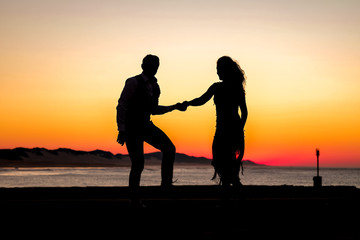 Fototapeta na wymiar Couple dancing on the pier during sunrise make for awesome silhouettes
