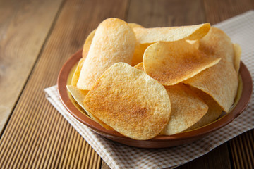 Potato chips in bowl and fresh potato. Delicious crispy snack. Rustic style.