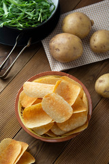 Potato chips in bowl and fresh potato. Delicious crispy snack. Rustic style.