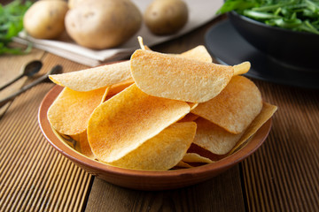 Potato chips in bowl and fresh potato. Delicious crispy snack. Rustic style.