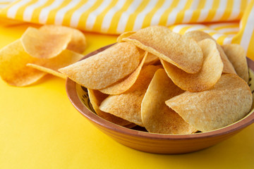 Potato chips in bowl on yellow background, top view
