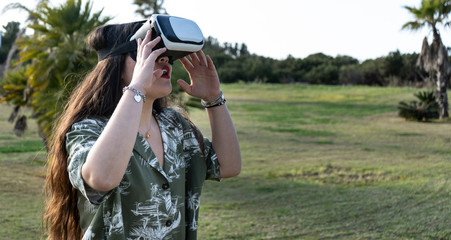 asian with virtual reality glasses in a park with grass and palm trees