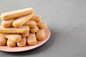 Savoiardi or ladyfingers cookies on pink plate on concrete background, side view. Copy space.